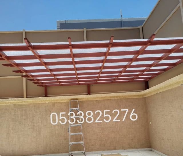 برجولة بعوارض حمراء وسقف لكسان شفاف فوق حوش منزل